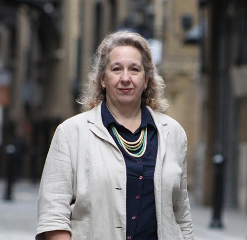 Woman in beige jacket and necklace.