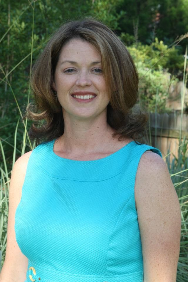 Woman in teal dress, smiling outdoors.